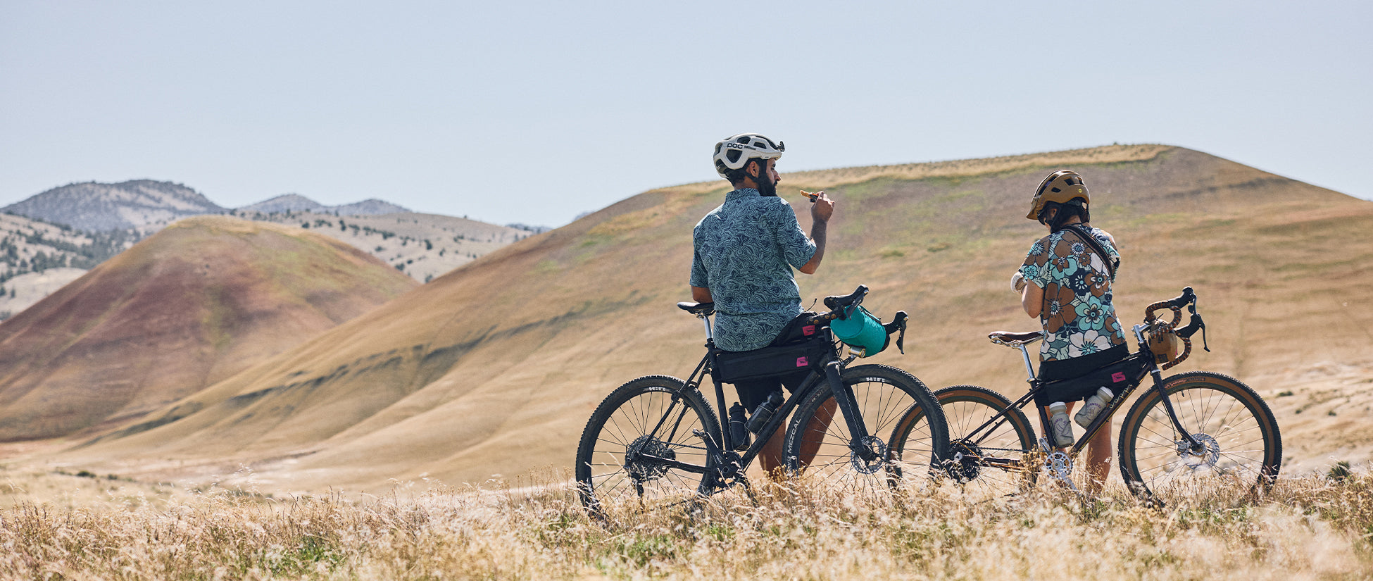 Two people sat by their bikes, looking out on a wide landscape