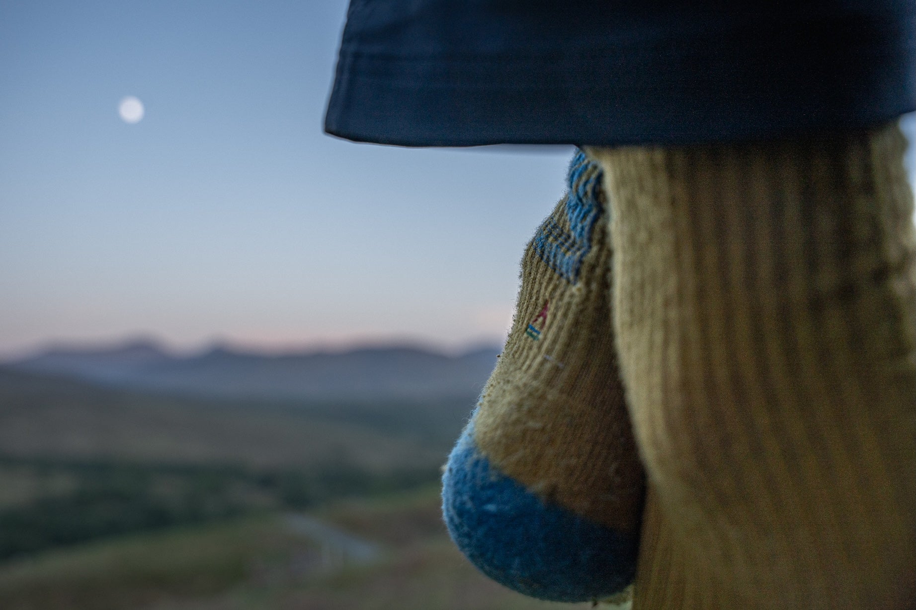 Close-up of a person's knitted socks with a mountainous landscape and moon in the background