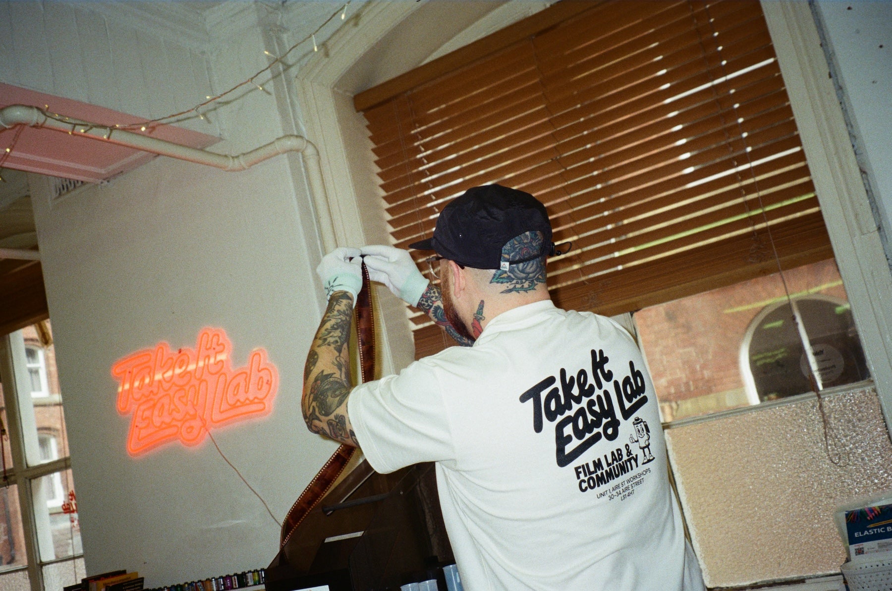 Person wearing a 'Take It Easy Lab' shirt in an indoor setting with a neon sign in the background.