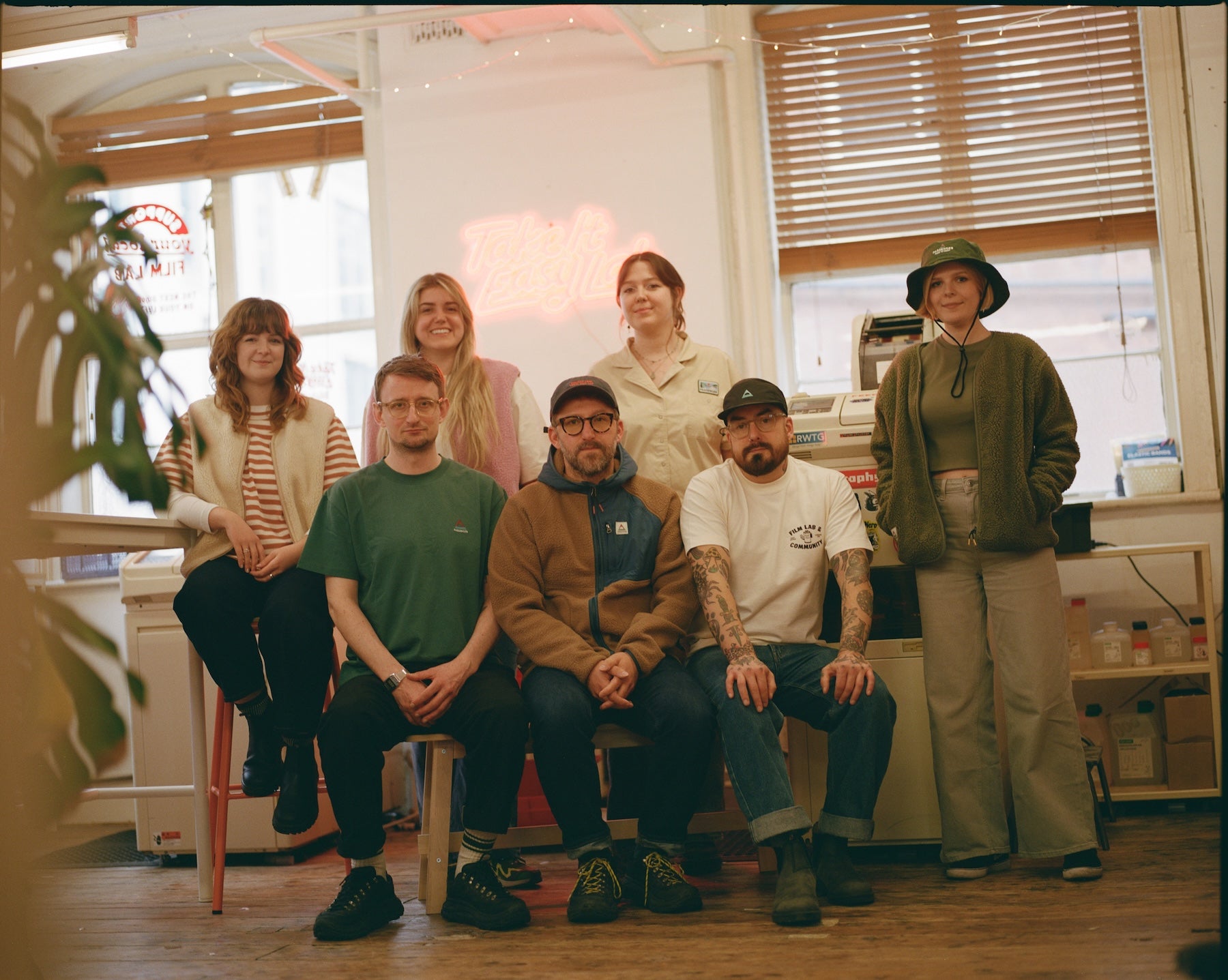Group of people posing together in a room with large windows.