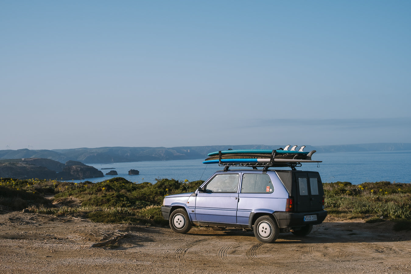 Car with surfboards on a roof rack parked near a scenic coastal area