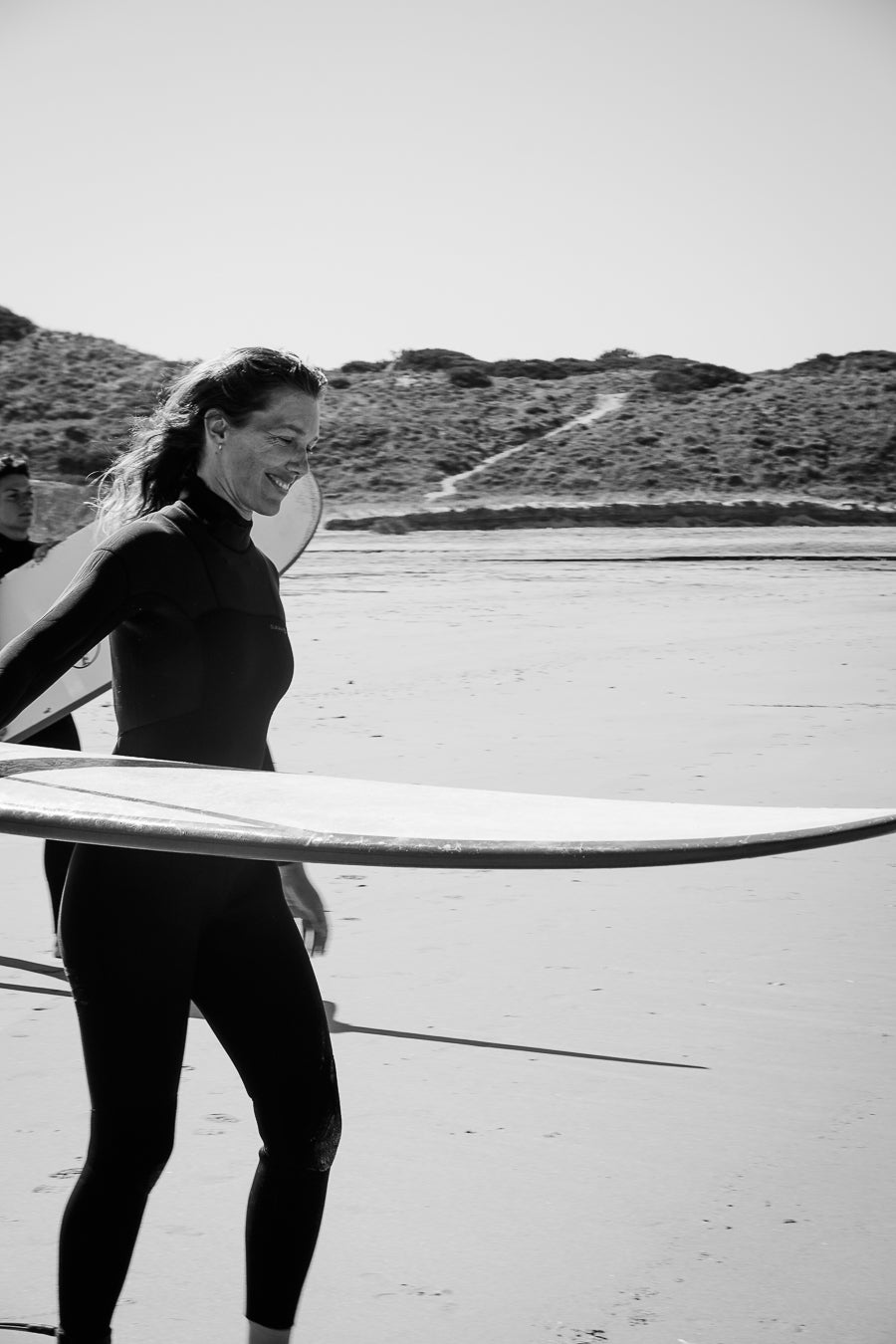 Person in a wetsuit holding a surfboard on a beach